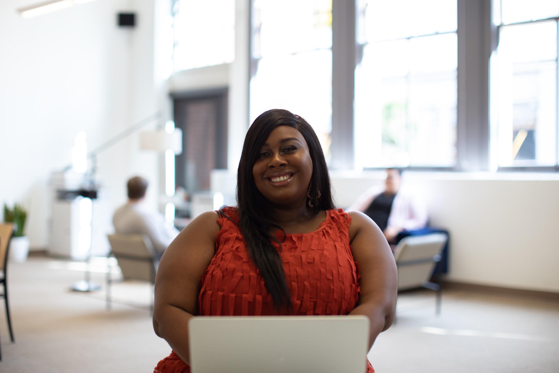 Person with long, dark hair wearing a sleeveless red shirt at a laptop