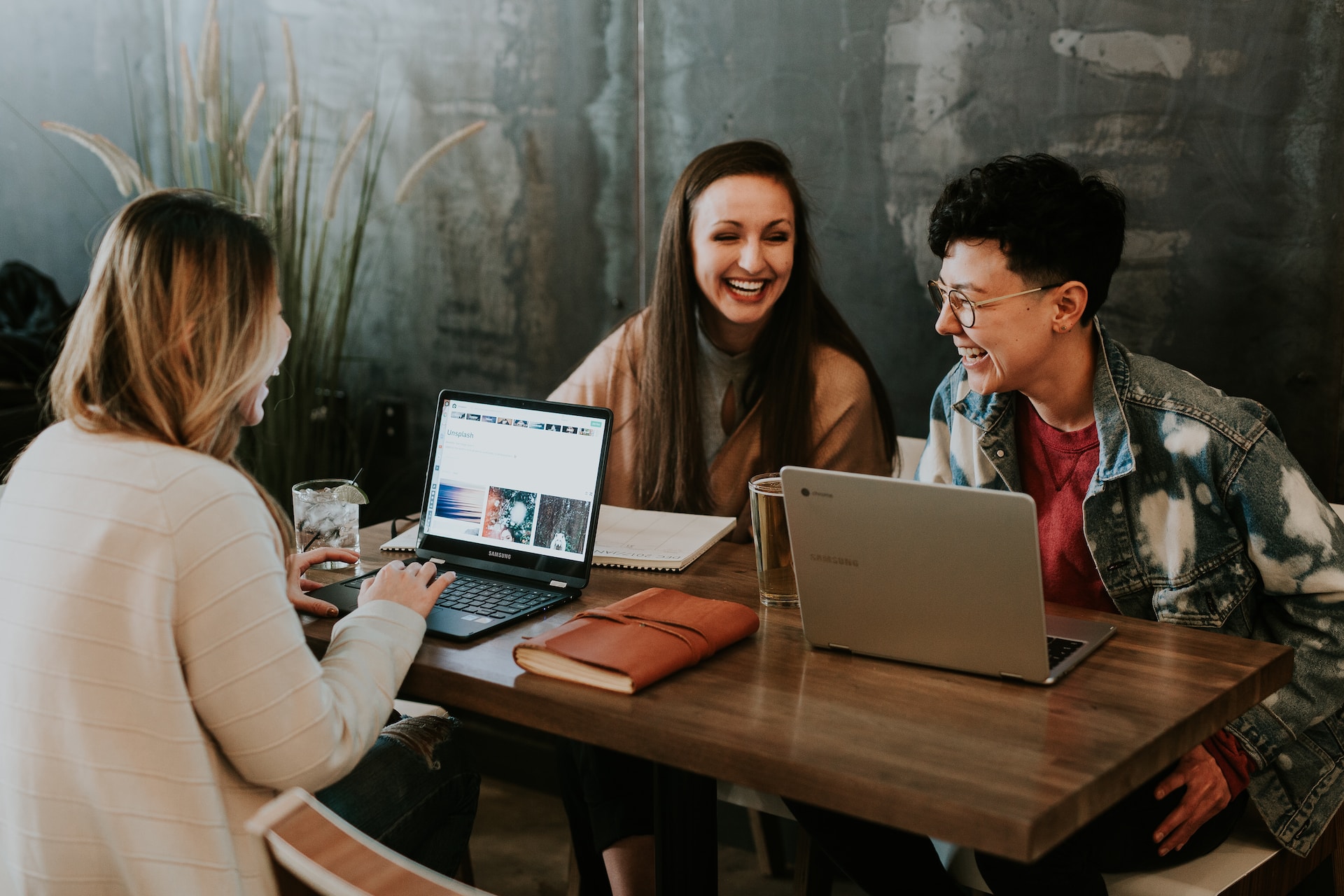 three people sitting around a table in front of laptops laughing