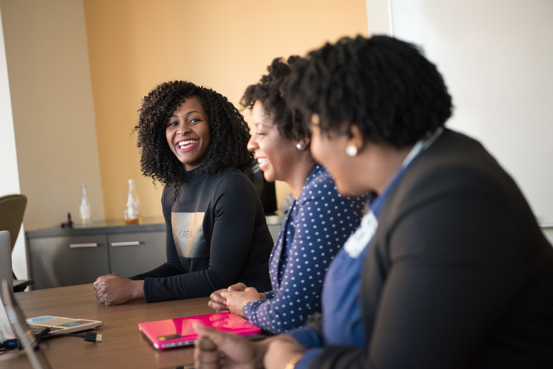 Three people sitting at a conference table, person on far end is smiling and looking toward the camera