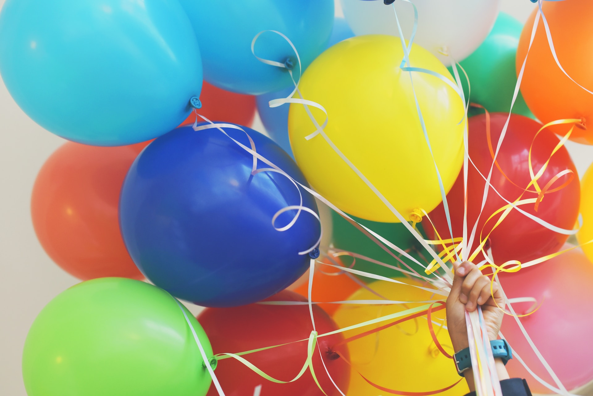 multi-colored balloons connected by ribbons and held by a hand. 