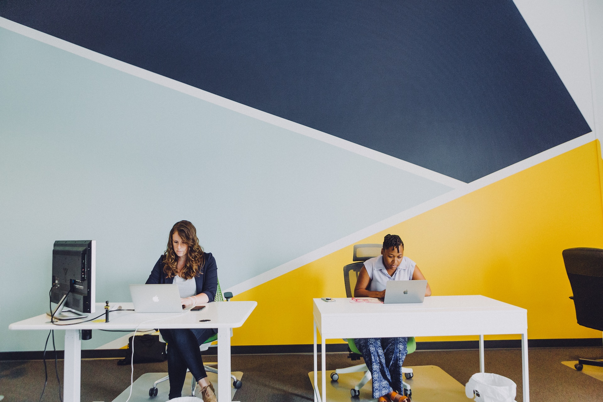 two workers sitting at desks against a wall with a bold pattern