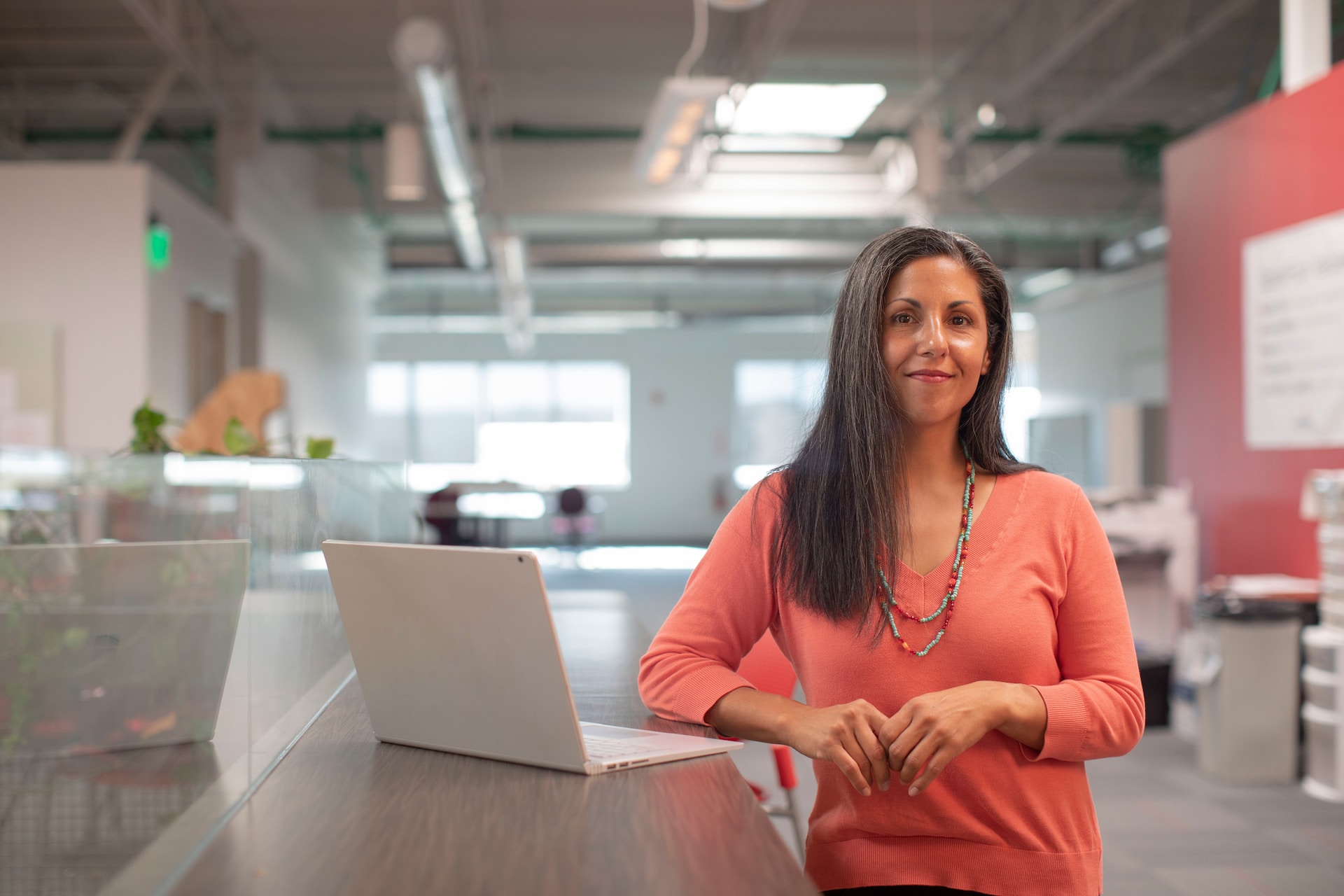 person in a peach-colored shirt standing by a laptop facing the camera