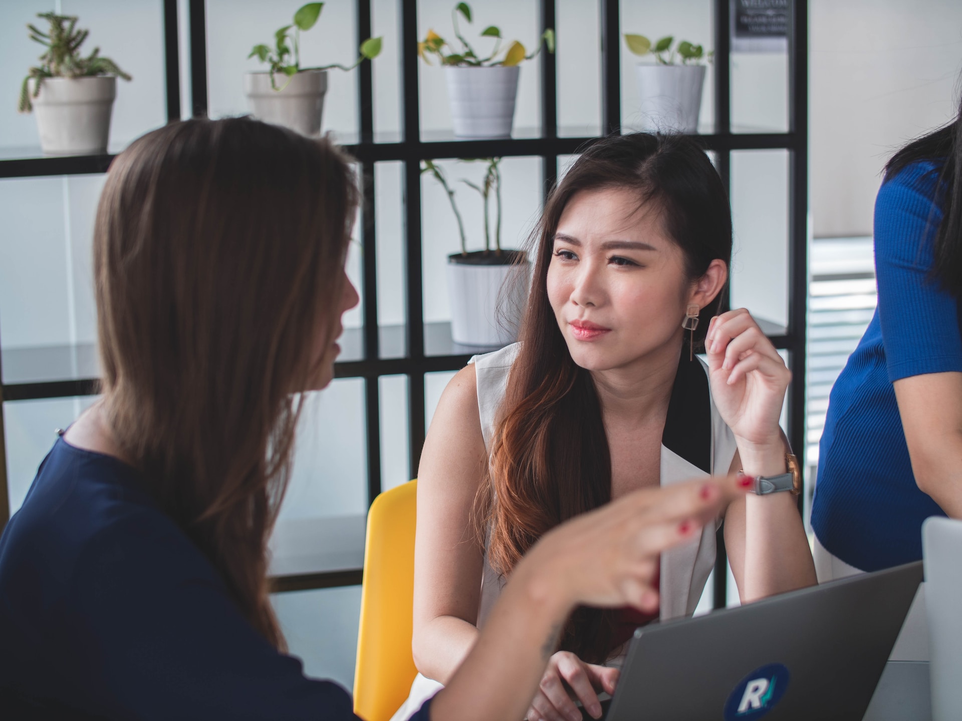 one woman sitting behind a laptop looking skeptically at another woman